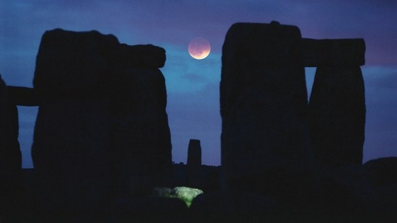 Apesar das nuvens e pancadas de chuva, a Lua brilha, eclipsada e avermelhada, durante o Eclipse Lunar Total, que aconteceu em maio de 2004. O nosso satélite natural ficou perfeitamente encaixado entre as pedras deste conhecido monumento ao Sol, em Stonehenge, na Inglaterra. No momento do registro fotográfico, a Lua estava a apenas cerca de 5 graus acima do horizonte, convenientemente localizada em uma das lacunas do círculo de pedras antigas