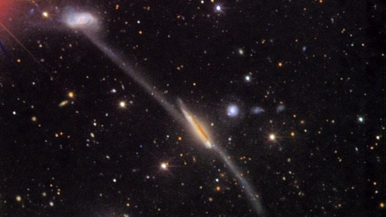 Uma ponte espetacular de estrelas e gás se estende por quase 250 mil anos-luz, juntando-se a este famoso par peculiar de galáxias catalogado como Arp 295. A ponte cósmica entre as galáxias e a longa cauda que se estende, abaixo e à direita do centro da imagem, evidenciam que estes sistemas estelares passaram próximos no passado, permitindo marés induzidas pela gravidade. Arp 295 fica a cerca de 270 milhões de anos-luz de distância, na direção da Constelação de Aquário