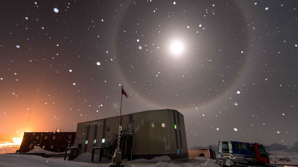 Você já viu um halo ao redor da Lua? Esses anéis de 22 graus ao redor da Lua – causados ​​pela queda de cristais de gelo na atmosfera da Terra – são um tanto raros. A imagem desta Lua Cheia em destaque foi tirada em julho de 2015, perto da estação Zhongshan, na Antártida. Visíveis em primeiro plano estão uma casa geradora de energia e um veículo para transporte sobre o gelo. Ao fundo, o que se parece com estrelas, na verdade, são flocos de neve iluminados perto da câmera