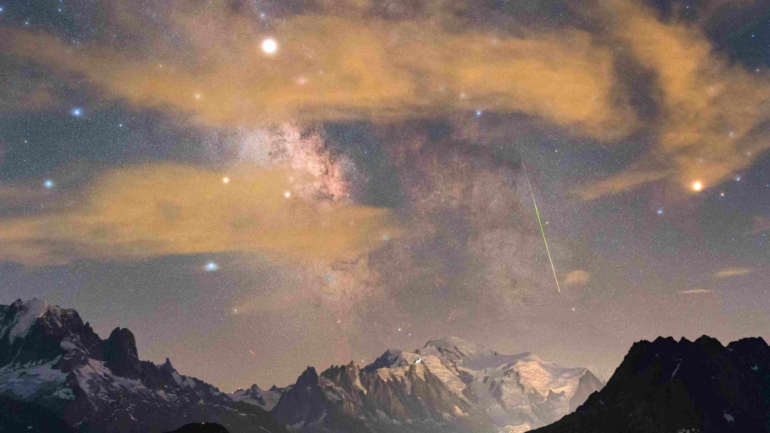 O nevado Mont Blanc é o destaque desta paisagem noturna, que retrata o ponto mais alto da Europa, nos Alpes Suíços. Nela, os campos estelares e as fendas escuras da Via Láctea aparecem acima da famosa montanha branca. Em meio à névoa, o brilhante planeta Saturno e a supergigante Antares (à direita), a estrela Alfa da Constelação de Escorpião, brilham através das nuvens que margeiam a região central da nossa galáxia. A cena de alta altitude, registrada em agosto de 2018, também inclui a trilha verde de um meteoro Perseida ao longo do plano galáctico