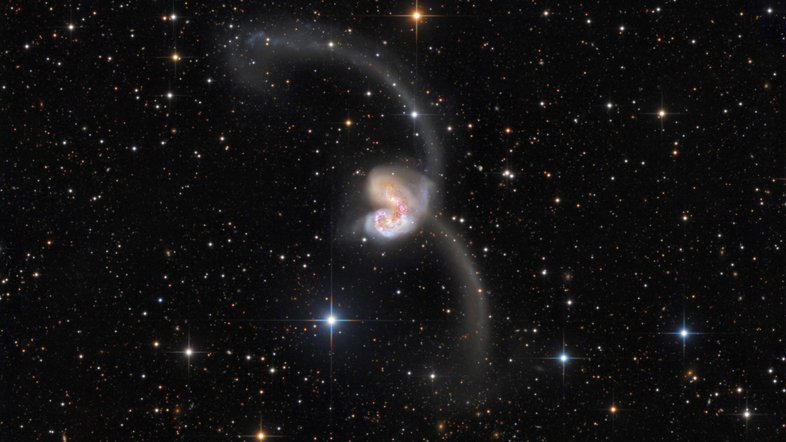 A cerca de 60 milhões de anos-luz de distância, na Constelação do Corvo, duas grandes galáxias estão em colisão. As estrelas das duas galáxias, catalogadas como NGC 4038 e NGC 4039, colidem muito raramente durante esse processo, que dura centenas de milhões de anos. Mas as grandes nuvens de gás molecular e poeira o fazem, desencadeando a formação de estrelas. Abrangendo mais de 500 mil anos-luz, esta imagem também revela novos aglomerados de estrelas e matéria lançada para longe do local pelas forças gravitacionais