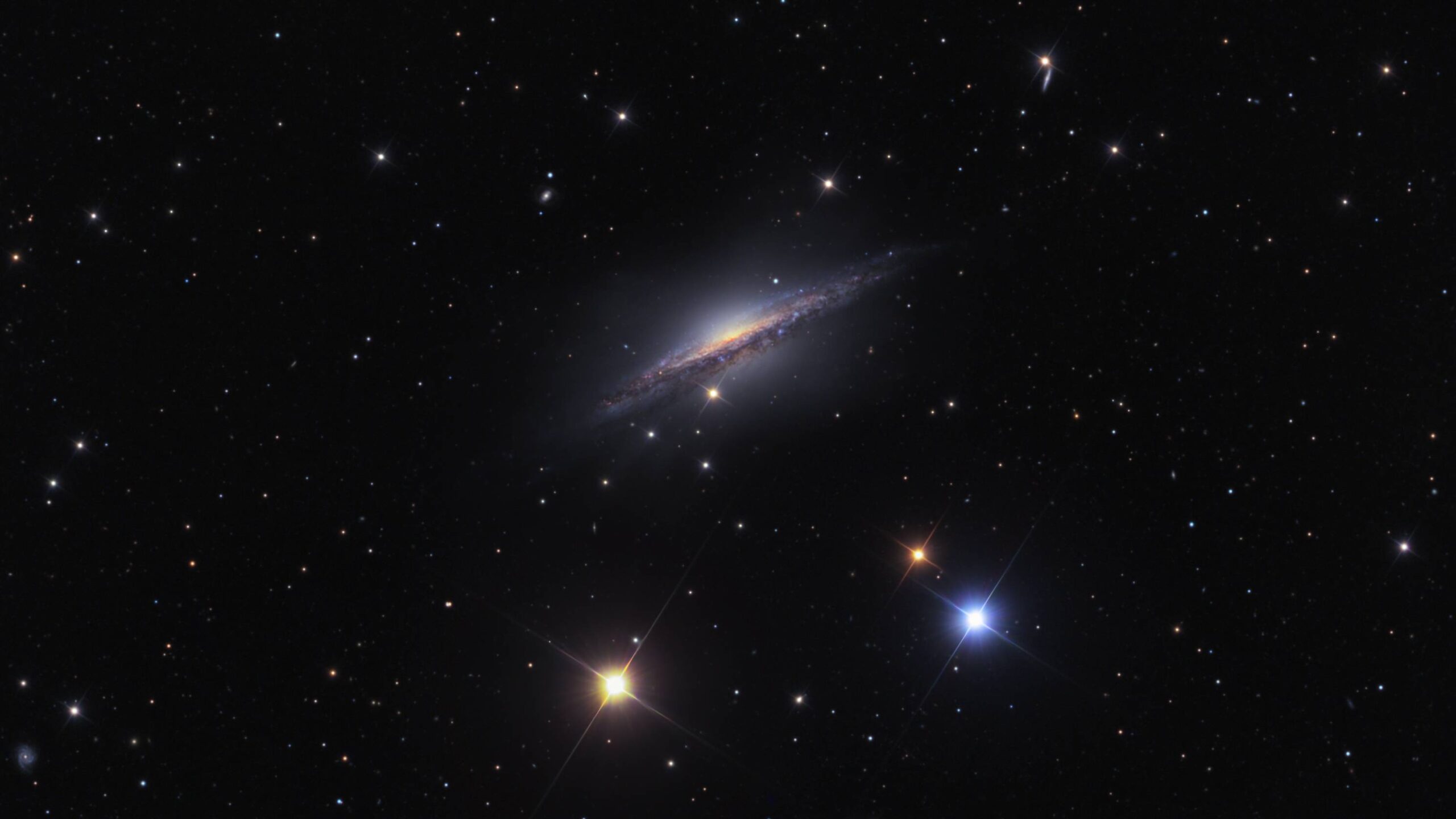 A grande e bela galáxia espiral NGC 1055 é o membro dominante de um pequeno grupo de galáxias a apenas 60 milhões de anos-luz de distância, na direção da Constelação de Cetus. Vista de lado, ela abrange cerca de 100 mil anos-luz, semelhante em tamanho à nossa Via Láctea. As estrelas coloridas e pontiagudas neste retrato cósmico da NGC 1055 estão em primeiro plano, dentro da nossa galáxia