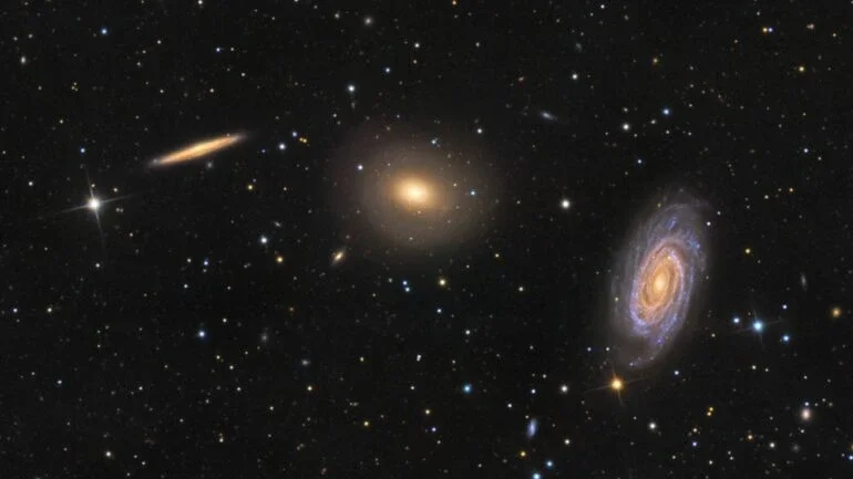 Este intrigante trio de galáxias está localizado na Constelação de Draco (“O Dragão”). Da esquerda para a direita estão a espiral vista de lado NGC 5981, a galáxia elíptica NGC 5982 e a espiral vista de frente NGC 5985. Todas estão a cerca de 100 milhões de anos-luz do planeta Terra. O núcleo brilhante da espiral frontal NGC 5985 mostra emissões proeminentes em comprimentos de onda específicos de luz, o que a torna uma Seyfert, um tipo de galáxia ativa. Esta exposição profunda também sugere conchas tênues em torno da elíptica NGC 5982, o que evidencia fusões galácticas no passado