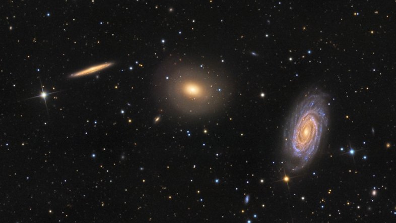 Este intrigante trio de galáxias está localizado na Constelação de Draco (“O Dragão”). Da esquerda para a direita estão a espiral vista de lado NGC 5981, a galáxia elíptica NGC 5982 e a espiral vista de frente NGC 5985. Todas estão a cerca de 100 milhões de anos-luz do planeta Terra. O núcleo brilhante da espiral frontal NGC 5985 mostra emissões proeminentes em comprimentos de onda específicos de luz, o que a torna uma Seyfert, um tipo de galáxia ativa. Esta exposição profunda também sugere conchas tênues em torno da elíptica NGC 5982, o que evidencia fusões galácticas no passado