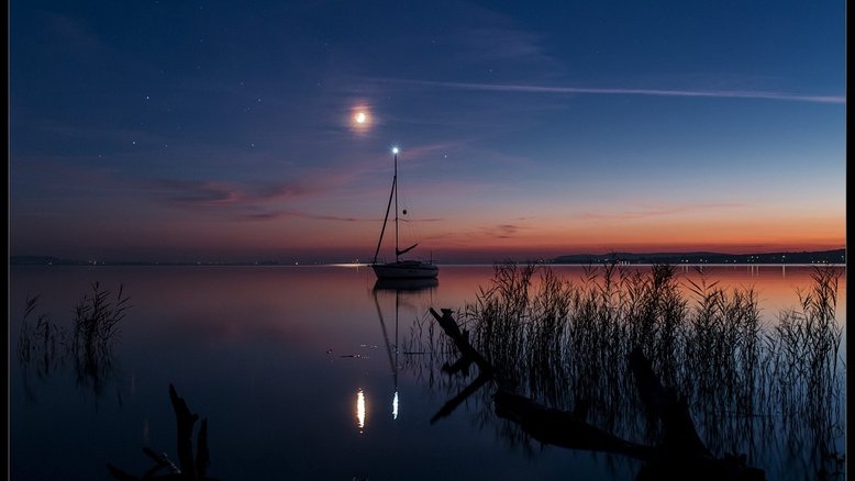 O planeta Marte, Antares (a estrela Alfa da Constelação de Escorpião), a Lua e o planeta Saturno são os faróis celestiais mais brilhantes neste céu sereno. A luz dourada do Sol ainda está espalhada ao longo do horizonte, capturada após o ocaso solar, em setembro de 2014. Na perspectiva do fotógrafo que registrou esta imagem das águas calmas do Lago Balaton, na Hungria, a luz de mastro de veleiro completa a cena. A luz do mastro, a estrela brilhante, os planetas e a Lua estão todos posando perto do plano da eclíptica