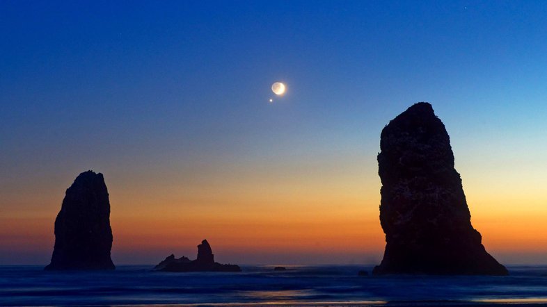 Nesta imagem, a Lua Nova passou lentamente por Vênus, aparecendo apenas a um grau de distância, no seu ponto mais próximo. Esse belo par celestial foi capturado em Cannon Beach, acima de uma formação rochosa na costa de Oregon (EUA), conhecida como Needles. Cerca de uma hora depois de esta imagem ter sido registrada, a rotação da Terra fez com que Vênus e a Lua se pusessem, ficando abaixo do horizonte visível, a Oeste