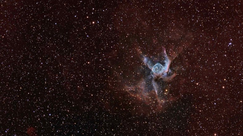 O objeto celeste que recebeu a alcunha de Capacete de Thor (NGC 2359) aparece em destaque nesta paisagem, localizada a cerca de 15 mil anos-luz, na Constelação do Cão Maior. Com tamanho heróico até para um deus nórdico, o Capacete de Thor tem cerca de 30 anos-luz de diâmetro. Semelhante a uma bolha interestelar, ele é resultado dos ventos rápidos de uma estrela massiva e brilhante, localizada perto do centro de uma nuvem molecular. Definida como do tipo Wolf-Rayet, essa estrela central é uma gigante extremamente quente, que está em um breve estágio de evolução pré-supernova