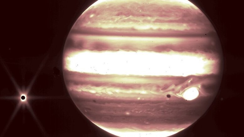 Nesta imagem em infravermelho, feita pelo Telescópio Espacial James Webb, Júpiter aparece ao lado da sua lua Europa, à esquerda. A Grande Mancha Vermelha está visível, em branco, à direita. A icônica mancha de Júpiter ficou branca devido à forma como a imagem infravermelha do Webb foi processada. A mancha escura, à esquerda da Grande Mancha Vermelha, é a sombra projetada de Europa na superfície de Júpiter