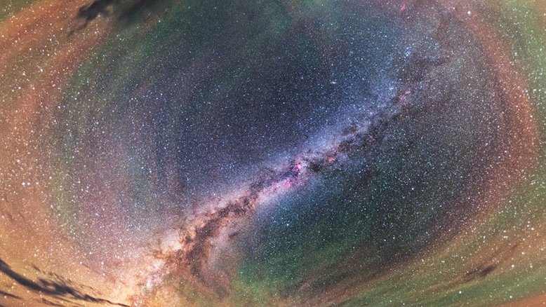 Este brilhante arco-íris com padrões repetitivos chama-se luminescência atmosférica. Nele, uma perturbação, como uma tempestade se aproximando, pode causar ondulações perceptíveis na atmosfera da Terra. Essas ondas gravitacionais são oscilações no ar análogas às criadas quando uma pedra é jogada em águas calmas. A luminescência atmosférica vermelha provavelmente se origina de moléculas de hidroxila, a cerca de 87 quilômetros de altitude, excitadas pela luz ultravioleta do Sol. A de cor laranja e verde, por sua vez, é causada por átomos de sódio e oxigênio um pouco mais acima. A paisagem desta imagem fica perto do Lago Keluke, na província de Qinghai, na China, exibindo a faixa central da Via Láctea como destaque