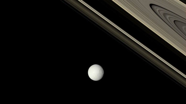 Qual a idade dos anéis de Saturno? Ninguém sabe ao certo. Uma possibilidade é que os anéis se formaram recentemente na história do nosso Sistema Solar, há apenas cerca de 100 milhões de anos, quando um objeto do tamanho de uma lua se despedaçou perto de Saturno. Evidências mais recentes, no entanto, levantam a possibilidade de que alguns dos anéis podem ter bilhões de anos e, portanto, serem tão antigos quanto o próprio planeta. Nesta imagem, os anéis de Saturno foram fotografados em suas cores verdadeiras pela sonda robótica Cassini. A brilhante e gelada Tétis, uma das luas de Saturno, aparece em primeiro plano, iluminada provavelmente por um jato de gelo vindo de sua lua irmã, Encélado