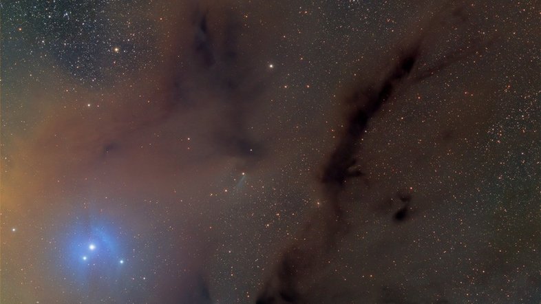 A poeira escura iluminada pela amarela e brilhante Antares, a estrela Alfa da Constelação de Escorpião, é o destaque desta paisagem. A faixa central da nossa Via Láctea conecta-se a Antares por meio de fluxos de poeira que receberam o nome de Rio Escuro. A região com nós de poeira mais densos, na parte inferior da imagem, é conhecida como B44. À esquerda, está Antares que, por ser tão brilhante, a poeira retratada reflete sua luz. A luz da estrela azul, também à esquerda, cria uma nebulosa de reflexão azulada ao seu redor, chamada IC 4605. B44 e IC 4605 ficam a cerca de 500 anos-luz de distância, na direção da Constelação de Escorpião (Foto: Thomas V. Davis)