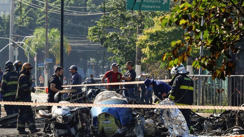 Destroços do avião aparecem carbonizados no chão. Ao redor, estão bombeiros e policiais que trabalharam no atendimento à ocorrência
