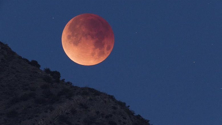 Nesta imagem, vê-se o registro de um Eclipse Lunar Total em janeiro de 2018, quando a Lua deslizou pela sombra do planeta Terra. Esta foto telescópica captura a Lua totalmente eclipsada, enquanto ela se punha acima do horizonte ocidental e das Montanhas Chiricahua do Sul, no Arizona. O tom avermelhado da Lua é devido à luz solar espalhada na sombra da Terra. Ainda assim, a sombra do planeta visivelmente fica mais escura perto do centro, em direção ao topo do disco lunar