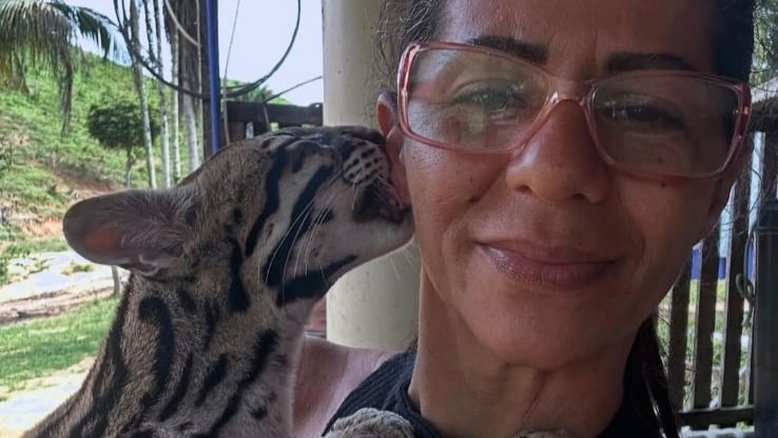 Fotografia da influenciadora Luciene Candido com a jaguatirica batizada por ela de "Pituca". O felino parece dar um beijo na bochecha da mulher