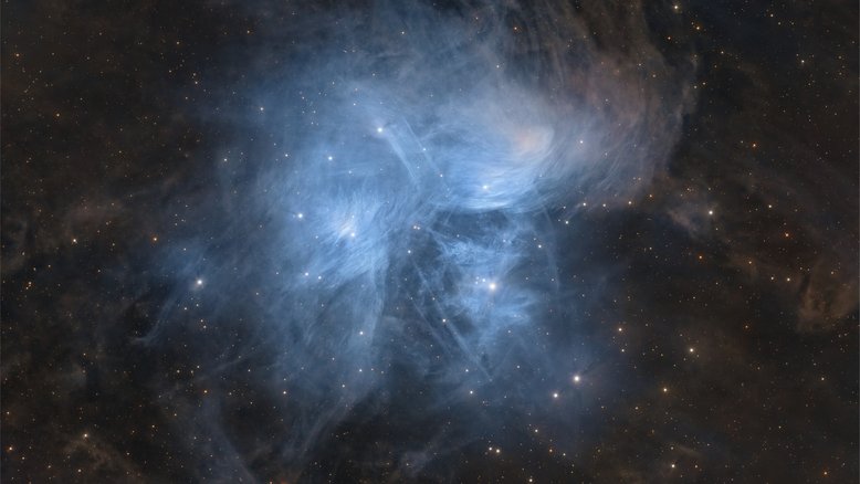 A apenas 400 anos-luz de distância, o encantador aglomerado aberto de estrelas das Plêiades, ou Sete Irmãs, é famoso por suas impressionantes nebulosas de reflexão azuis. Localizado na Constelação de Touro, suas estrelas estão nas dependências do Braço de Órion da nossa galáxia, a Via Láctea. As estrelas irmãs, no entanto, não estão relacionadas à nuvem de poeira. Elas apenas passam pela mesma região do espaço. Na mitologia grega, as Plêiades eram sete filhas do titã astronômico Atlas e da ninfa do mar Pleione. Os nomes de seus pais estão incluídos na lista das nove estrelas mais brilhantes do aglomerado