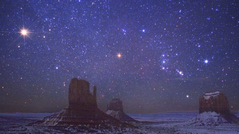 Esta paisagem do Monument Valley, nos EUA, destaca seus famosos montes compostos por rocha, após o efeito da erosão da água, em sua volta. O registro, feito em dezembro de 2007, traz o planeta Marte, à esquerda da paisagem celeste, como um farol brilhante e laranja, que é o objeto mais brilhante no quadro. À direita de Marte, está a Constelação de Órion. Betelgeuse é a estrela avermelhada, perto do centro, com o Cinturão de Órion e a Nebulosa de Órion, mais à direita. Ainda seguindo na mesma sequência, vê-se a brilhante estrela azul Rigel, bem acima do monte chamado de Merrick Butte
