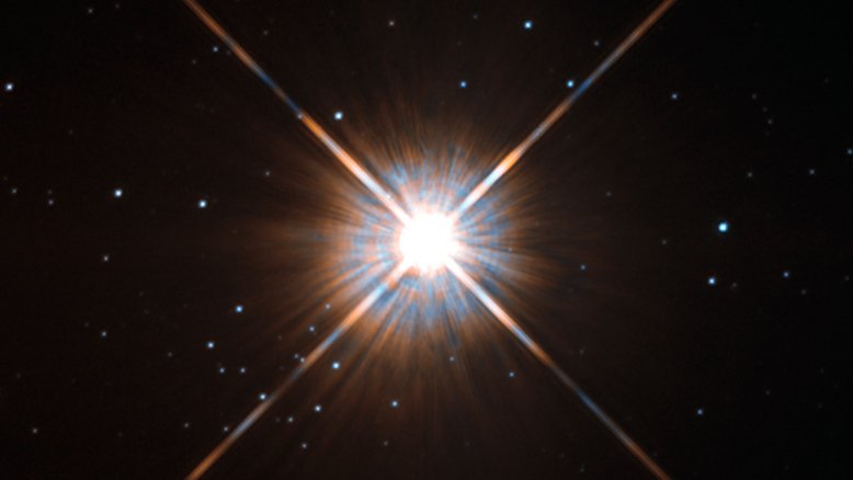 A estrela mais próxima à Terra, Proxima Centauri, é membro do sistema estelar Alpha Centauri. A sua luz leva apenas 4,24 anos para chegar até nós. Esta pequena estrela vermelha, no centro da imagem feita pelo Telescópio Espacial Hubble, é tão tênue que só foi descoberta em 1915. Picos de difração, em forma de X e criados pelo telescópio, circundam Proxima Centauri, enquanto várias estrelas mais distantes em nossa Via Láctea estão visíveis ao fundo. A estrela mais brilhante do sistema Alpha Centauri é bastante semelhante ao nosso Sol, sendo conhecida há muito tempo, já que é a terceira estrela mais brilhante do céu noturno