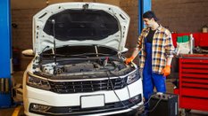 full length shot of handsome auto mechanic charging the battery using wire cables in modern service station