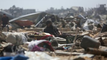 Um homem deitado sobre objetos recuperados observa palestinos inspecionarem barracas de um campo de deslocados que foram destruídas por bombardeios israelenses, perto de Khan Yunis, no sul da Faixa de Gaza, em 11 de julho de 2025 - AFP