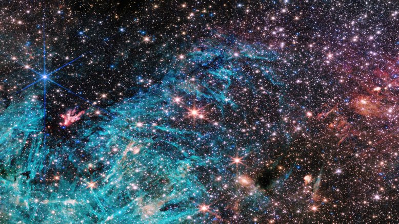 Nesta imagem, feita pelo Telescópio Espacial James Webb, vê-se uma parte do núcleo denso da Via Láctea, sob uma nova luz. Estima-se que 500 mil estrelas brilhem nesta imagem de Sagitário C (Sgr C), uma região de formação estelar a cerca de 300 anos-luz de distância de Sagitário A (Sgr A*), o buraco negro supermassivo no centro da via Láctea, na direção da Constelação de Sagitário. Uma grande região de hidrogênio ionizado, mostrada em ciano, contém estruturas intrigantes em forma de agulha, sem qualquer orientação uniforme