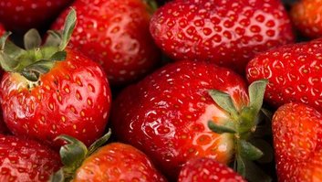 delicioso-morango-vermelho-maduro-maduro-com-folhas-verdes-na-mesa-escura
