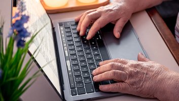 Retired woman uses laptop, hands close up.