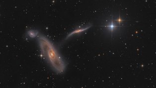 Este colorido campo de visão telescópico apresenta um trio de galáxias interagindo a quase 90 milhões de anos-luz de distância, na direção da Constelação de Virgem. À direita, estão duas estrelas pontiagudas da Via Láctea, em primeiro plano. Com braços espirais extensos e faixas de poeira, o membro dominante do trio, NGC 5566, tem cerca de 150 mil anos-luz de diâmetro. Logo acima dela, está a menor e azulada NGC 5569. Perto do centro, uma terceira galáxia, NGC 5560, foi esticada e distorcida por sua interação com a massiva NGC 5566. O trio também está incluído no Atlas de Galáxias Peculiares de Halton Arp, como Arp 286