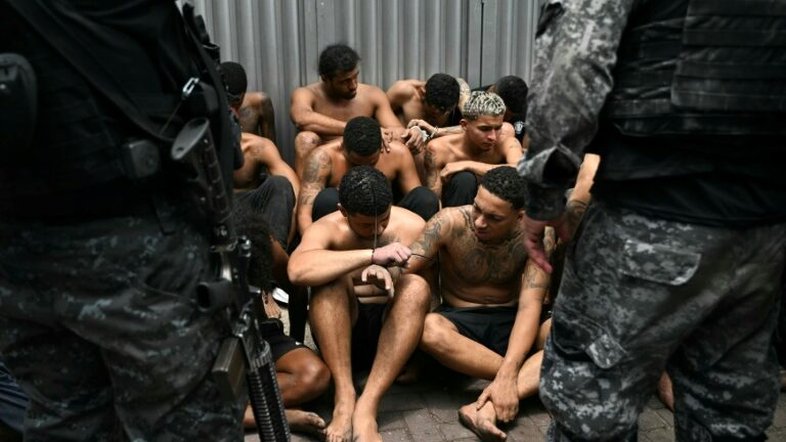 Policiais vigiam suspeitos de crimes presos durante a Operação Contenção na favela da Vila Cruzeiro, no Complexo da Penha, Rio de Janeiro, em 28 de outubro de 2025 - AFP