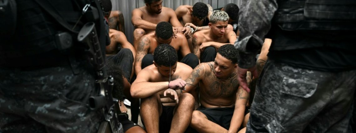 Policiais vigiam suspeitos de crimes presos durante a Operação Contenção na favela da Vila Cruzeiro, no Complexo da Penha, Rio de Janeiro, em 28 de outubro de 2025 - AFP