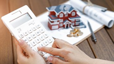 uma-mao-feminina-operando-uma-calculadora-na-frente-de-um-modelo-de-casa-de-villa