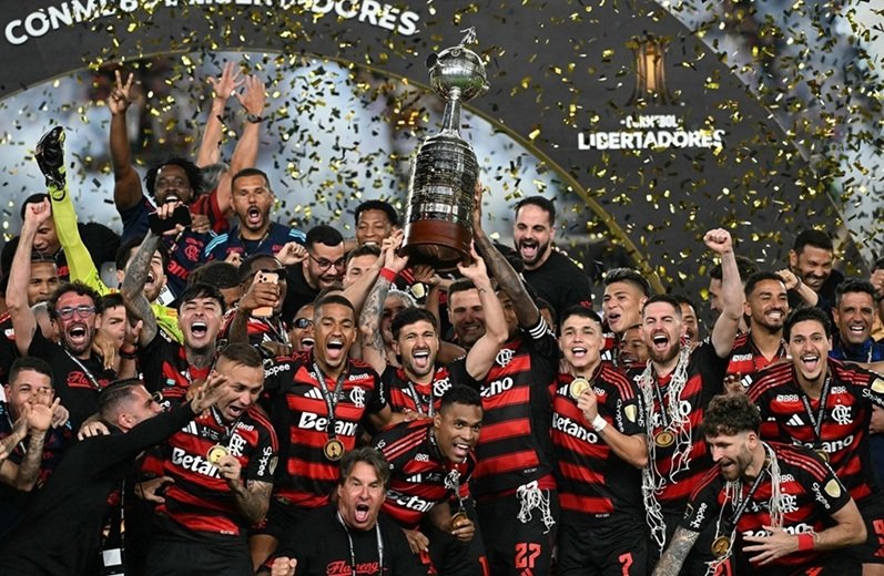 atacante #27 do Flamengo, Bruno Henrique (D), e o meio-campista uruguaio #10 Giorgian de Arrascaeta (E) levantam o troféu com os companheiros de equipe após vencerem a final brasileira da Copa Libertadores de futebol entre Palmeiras e Flamengo
